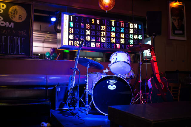 Drum set and electric guitar on stage at Love Bomb 2017 event supporting My Voice Music, illuminated with colorful lights.